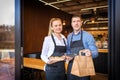 Small business owners couple standing in doorway of trendy restaurant delivering takeaway orders and attending customers Royalty Free Stock Photo